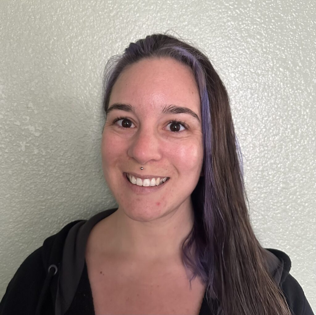Smiling person with purple highlights in hair.